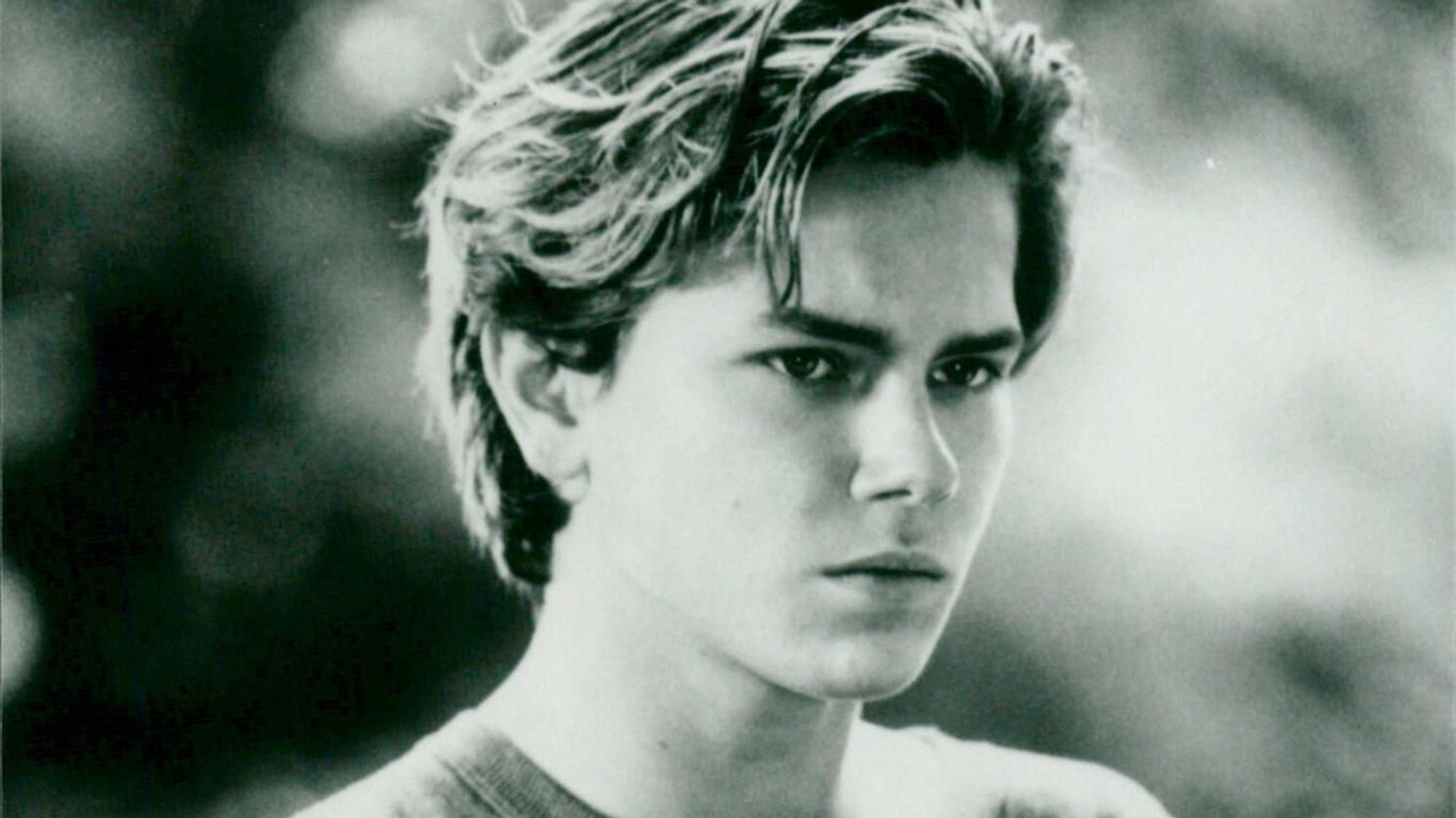 River Phoenix mit T-Shirt und ernster Miene. Eine Szene aus dem Film „Die Flucht ins Ungewisse“.