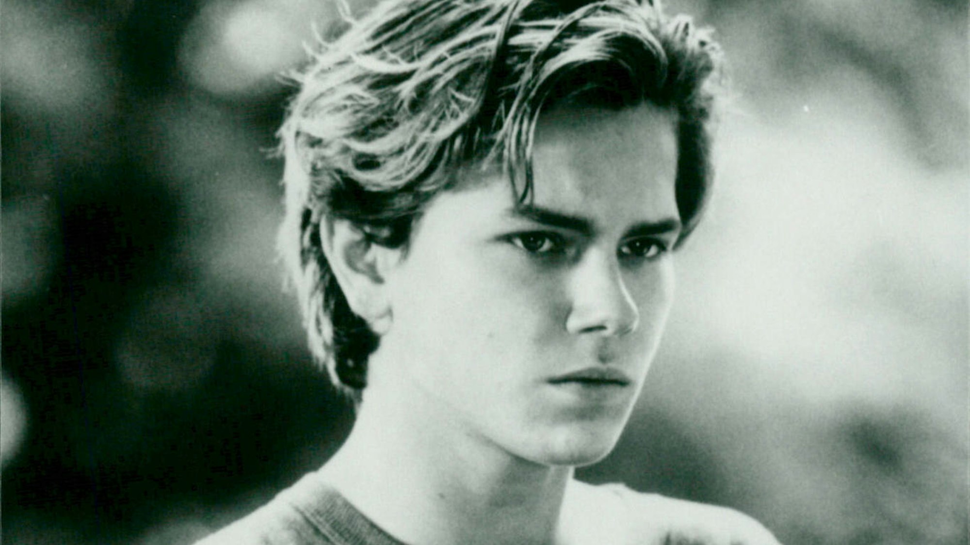 River Phoenix mit T-Shirt und ernster Miene. Eine Szene aus dem Film „Die Flucht ins Ungewisse“.