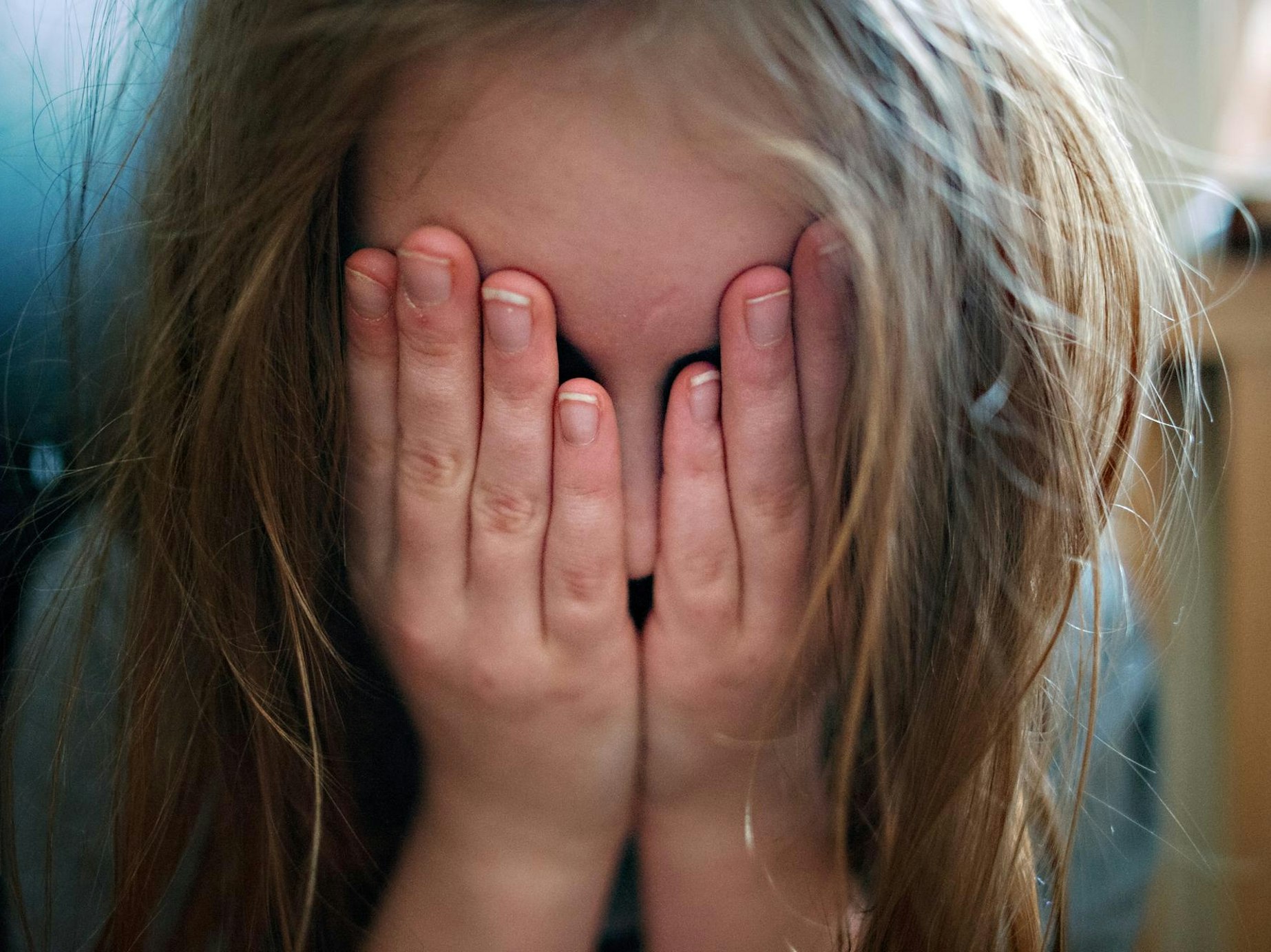 Ein Mädchen mit langen blonden Haaren hält sich verzweifelt die Hände vors Gesicht.