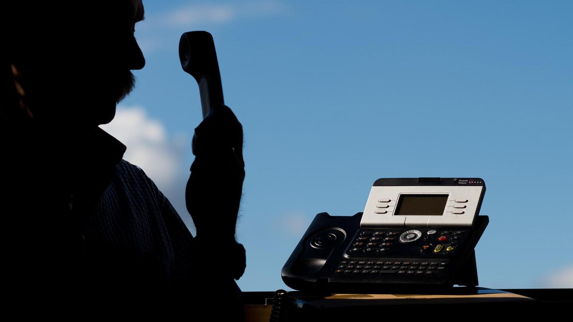 Auf dem Symbolbild ist die Silhouette eines Mannes am Telefon zu sehen.