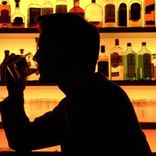 Eine Person sitzt an einer Bar und trinkt an einem Glas.