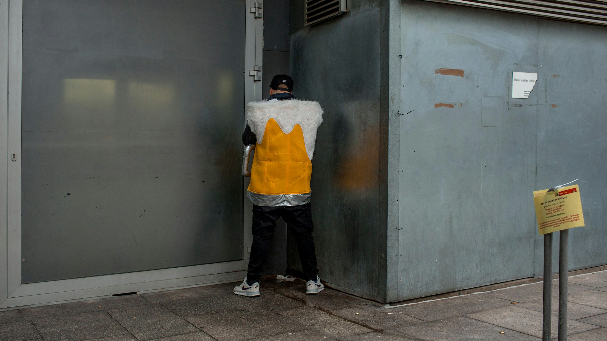 als Kölschglas verkleideter Mann pinkelt in einer Hausecke