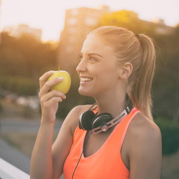 Eine Frau in Sportkleidung hält einen Apfel in der Hand.