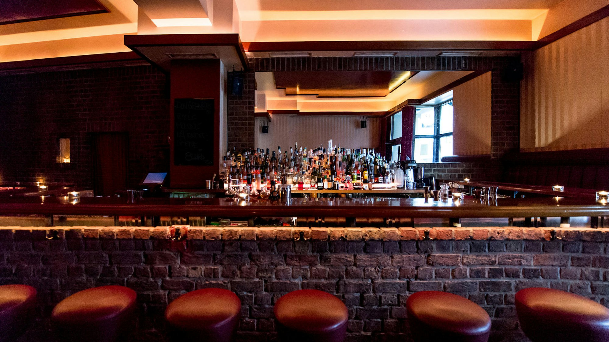 Barhocker stehen vor einem gemauerten Tresen, Getränkeflaschen im Hintergrund