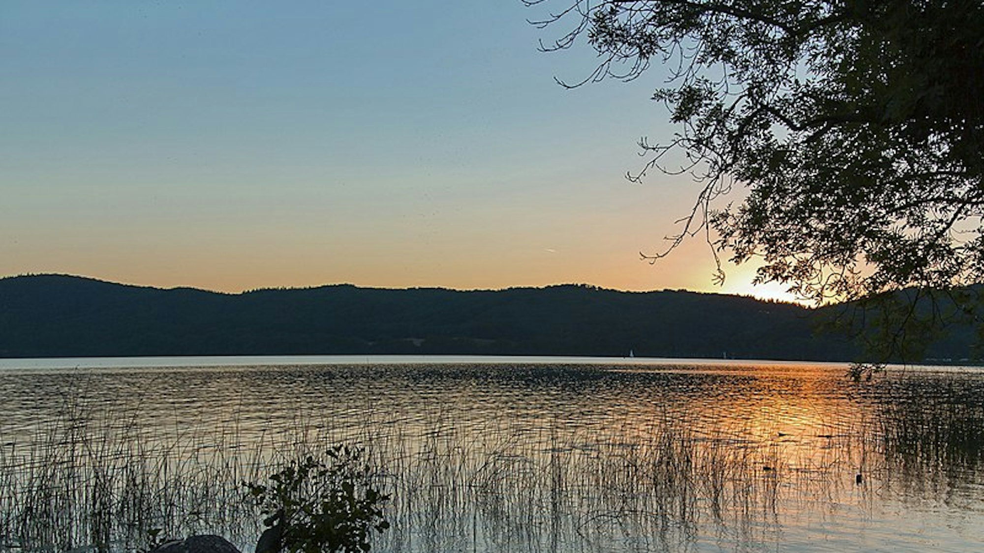 Hinter dem Laacher See geht die Sonne unter.