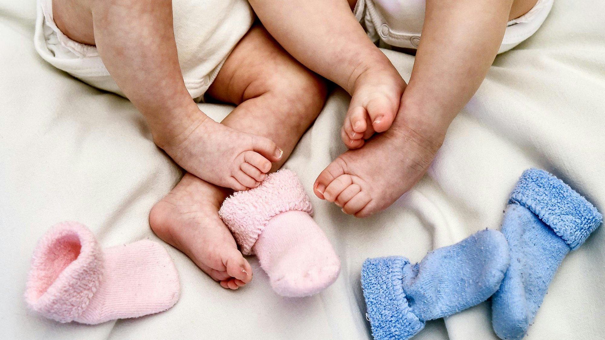 Zwei Babys liegen im Bett und zeigen ihre Füße.