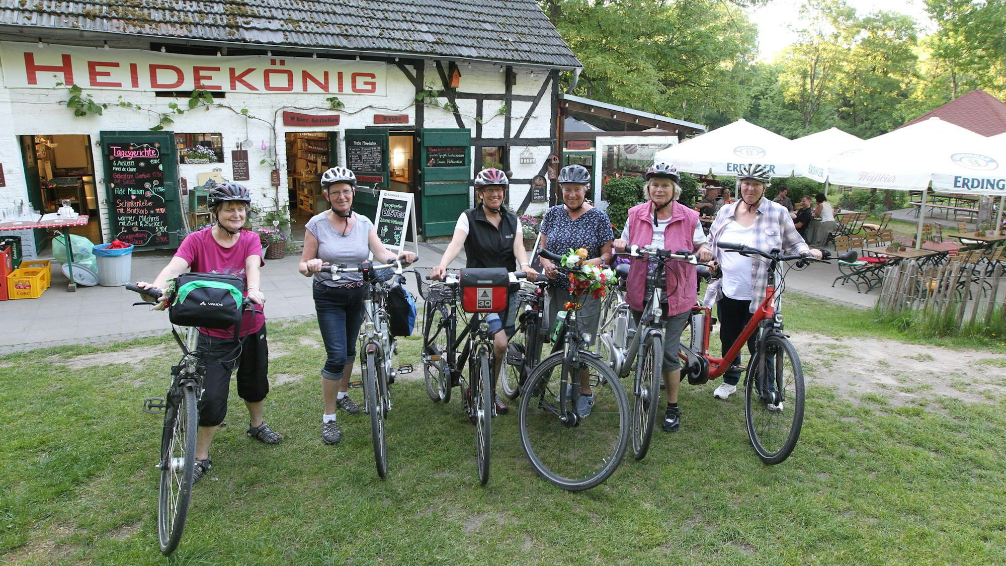 Eine Gruppe steht mit Fahrrädern vor einem Gebäude, auf dem in roten Buchstaben Heidekönig steht.