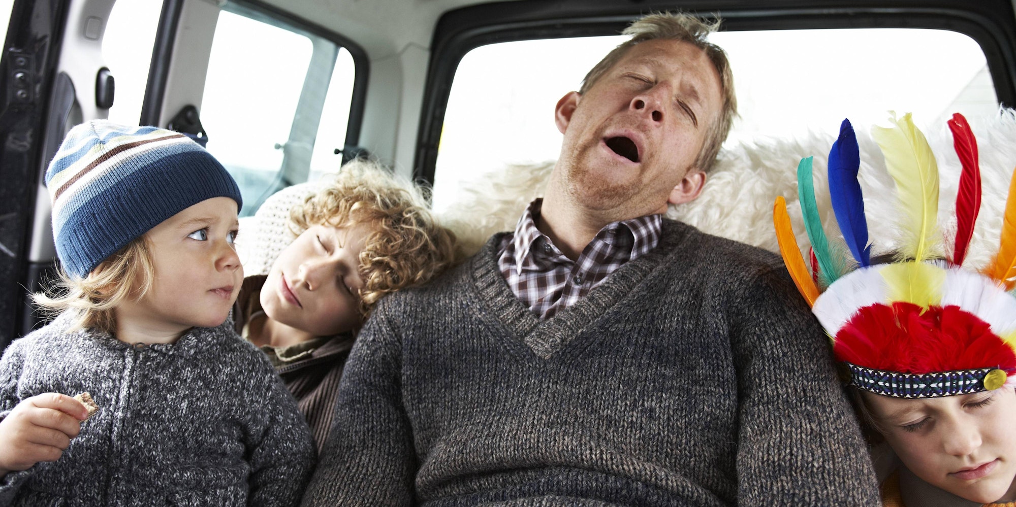 Müder Vater sitzt mit drei Kindern im Auto.