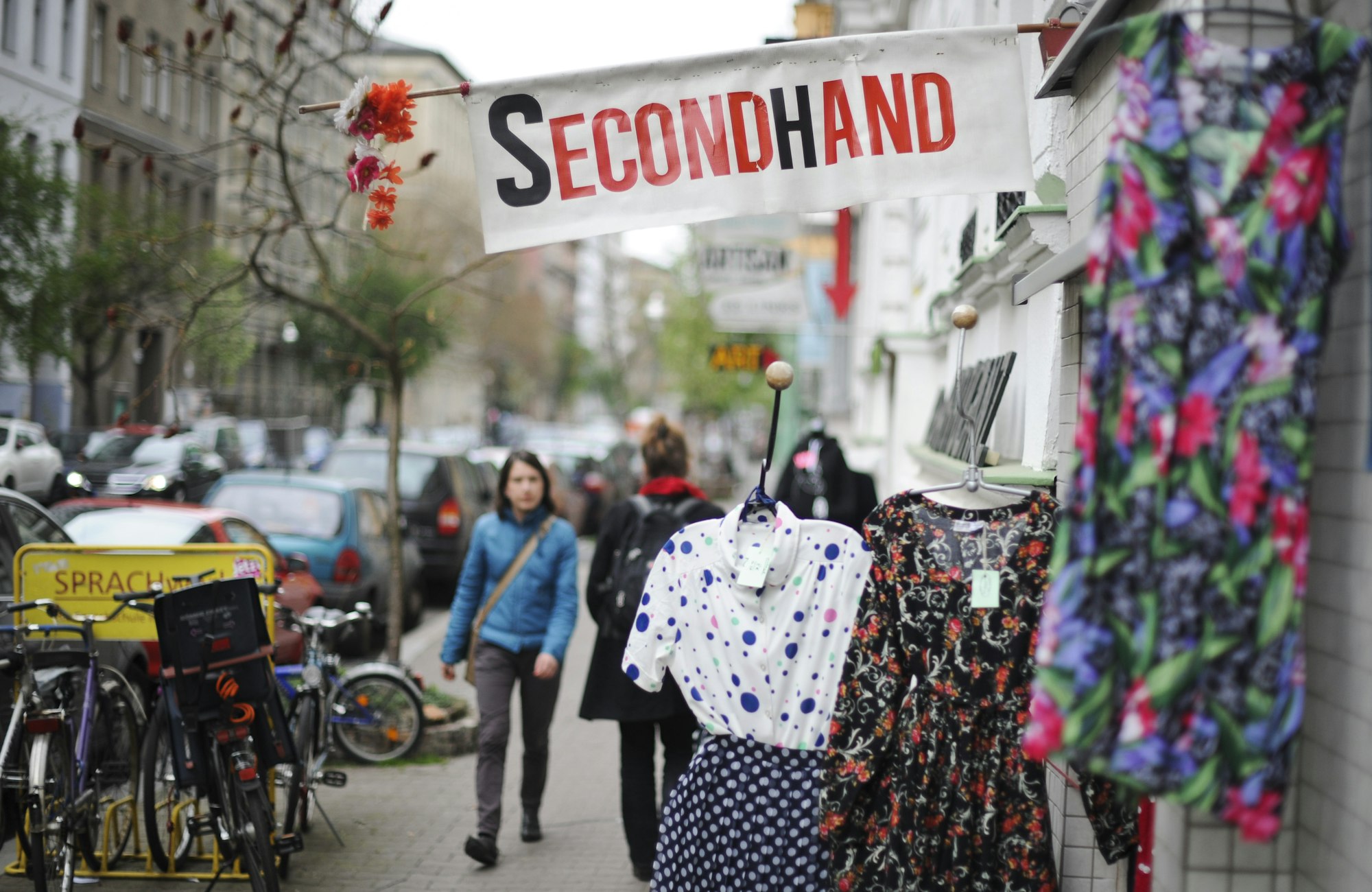 Das Schild eines Second Hand-Ladens ragt über einer Kleiderstange auf den Bürgersteig.