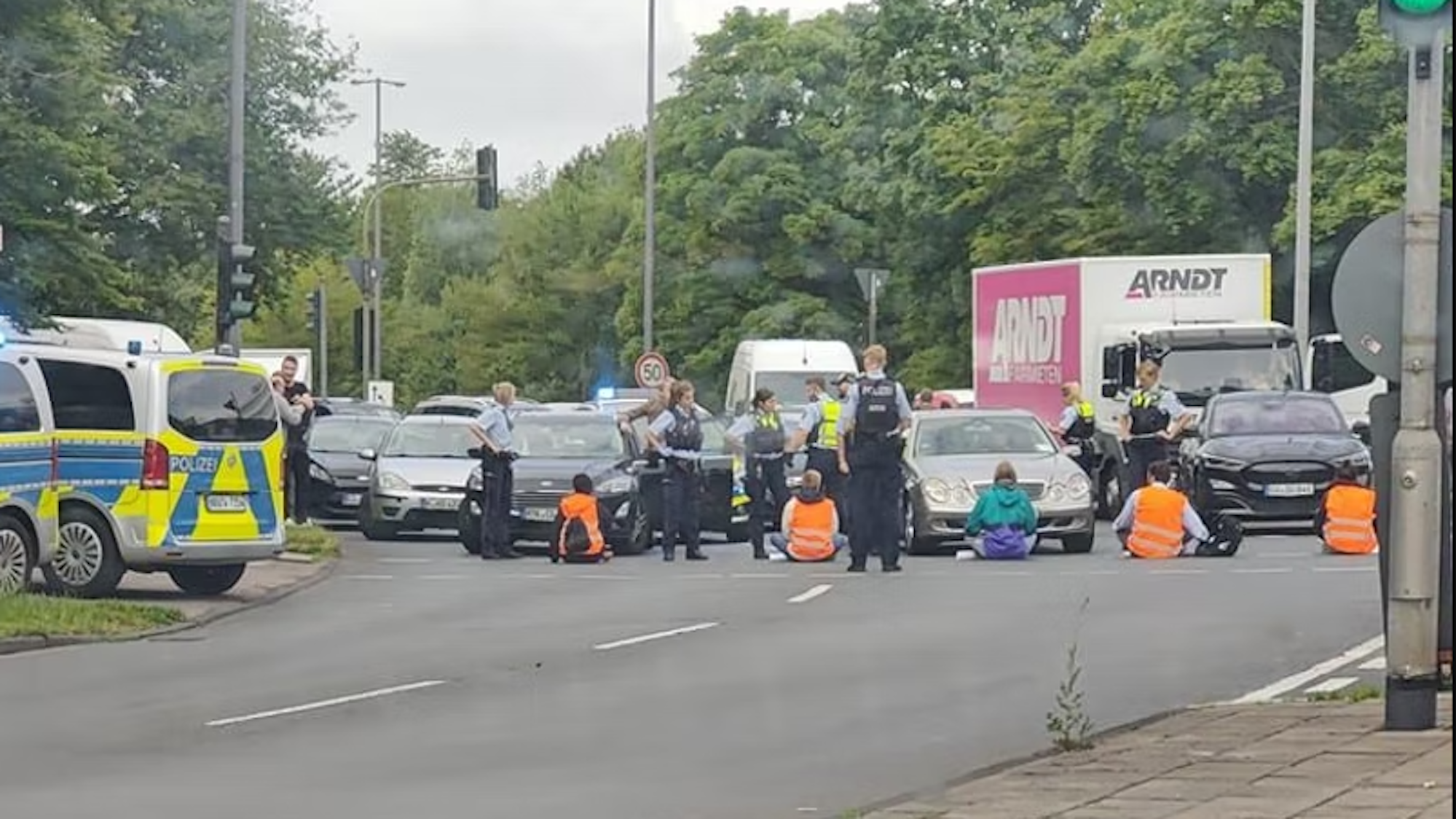 Fünf Menschen blockieren die zweispurige Hauptverkehrsstraße. An der Stelle mündet die stadteinwärts führende A57 in die Innere Kanalstraße.