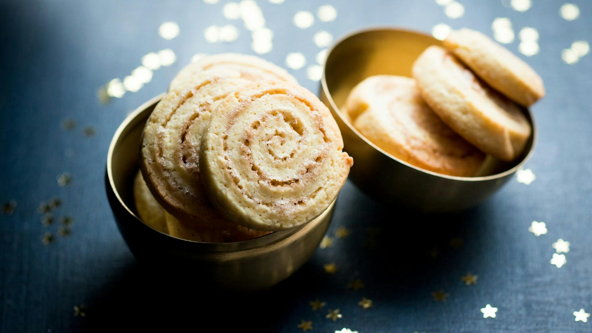 Zimtschnecken sind in goldenen Schüsselchen lecker angerichtet, rundherum liegen goldene Sternchen.