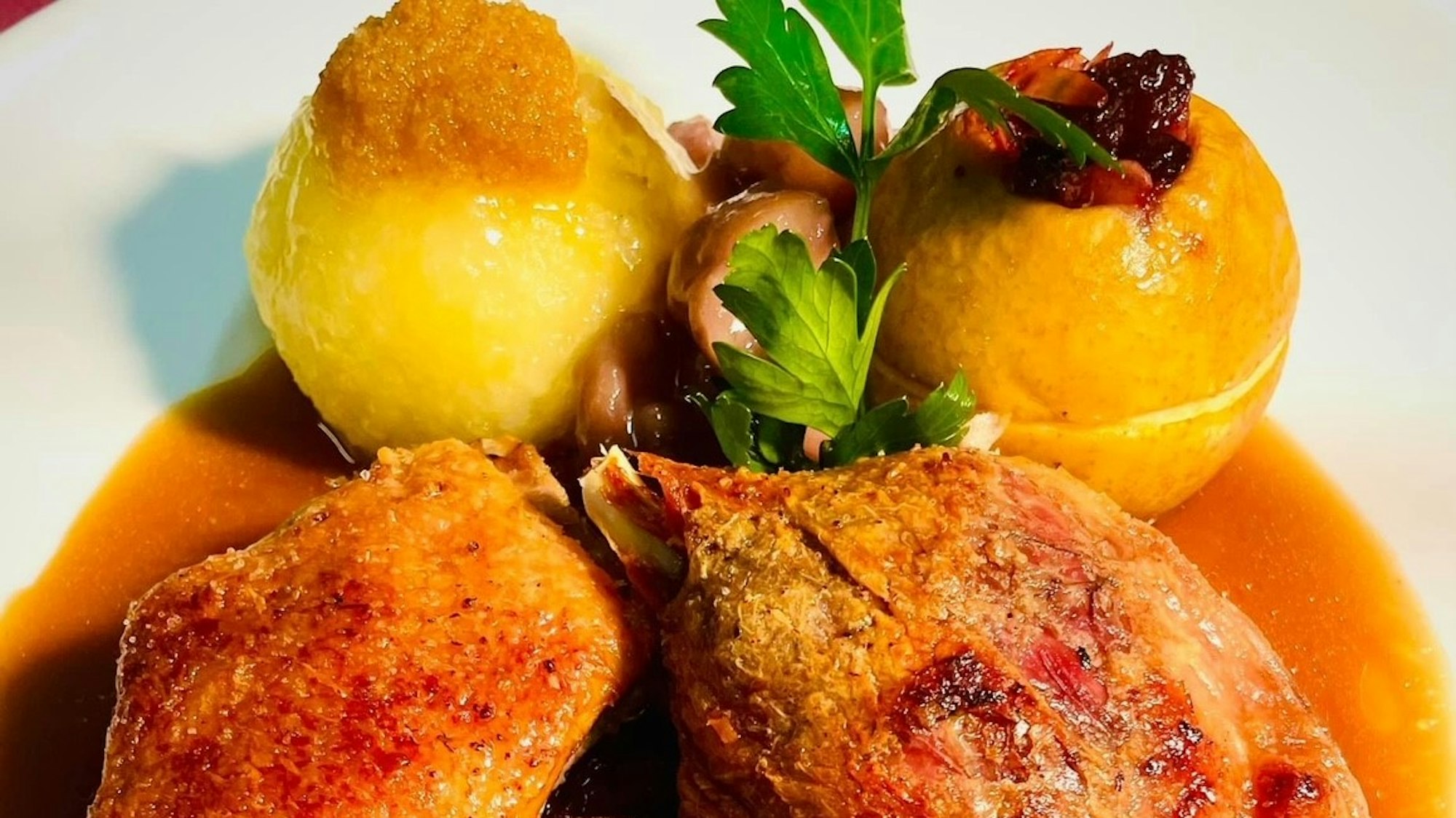 Eine Gänsekeule, angerichtet mit Kartoffelkloß und Bratapfel sowie Soße.