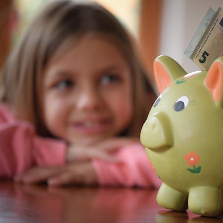 Kleines Mädchen schaut lächelnd auf Sparschwein