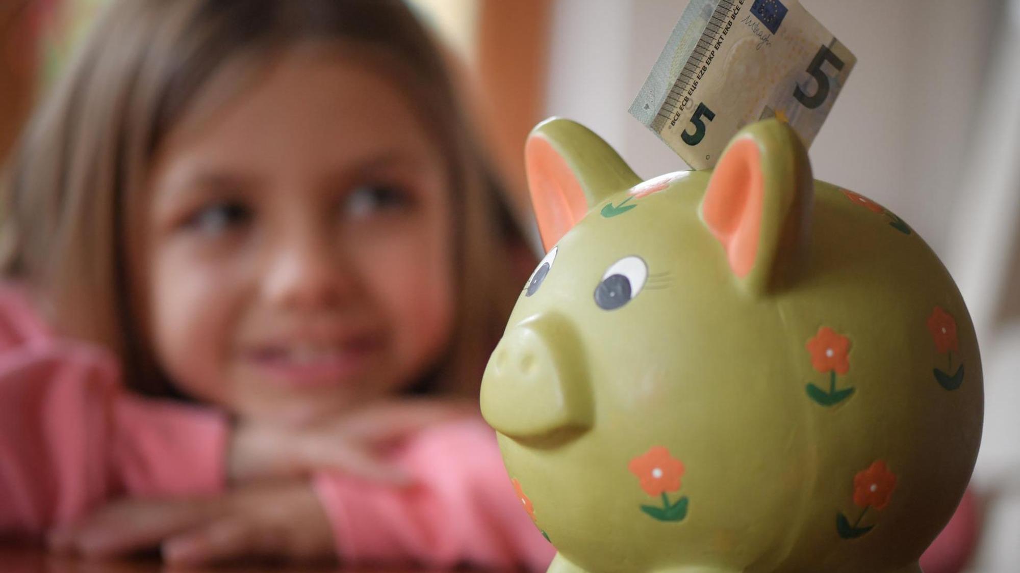 Kleines Mädchen schaut lächelnd auf Sparschwein