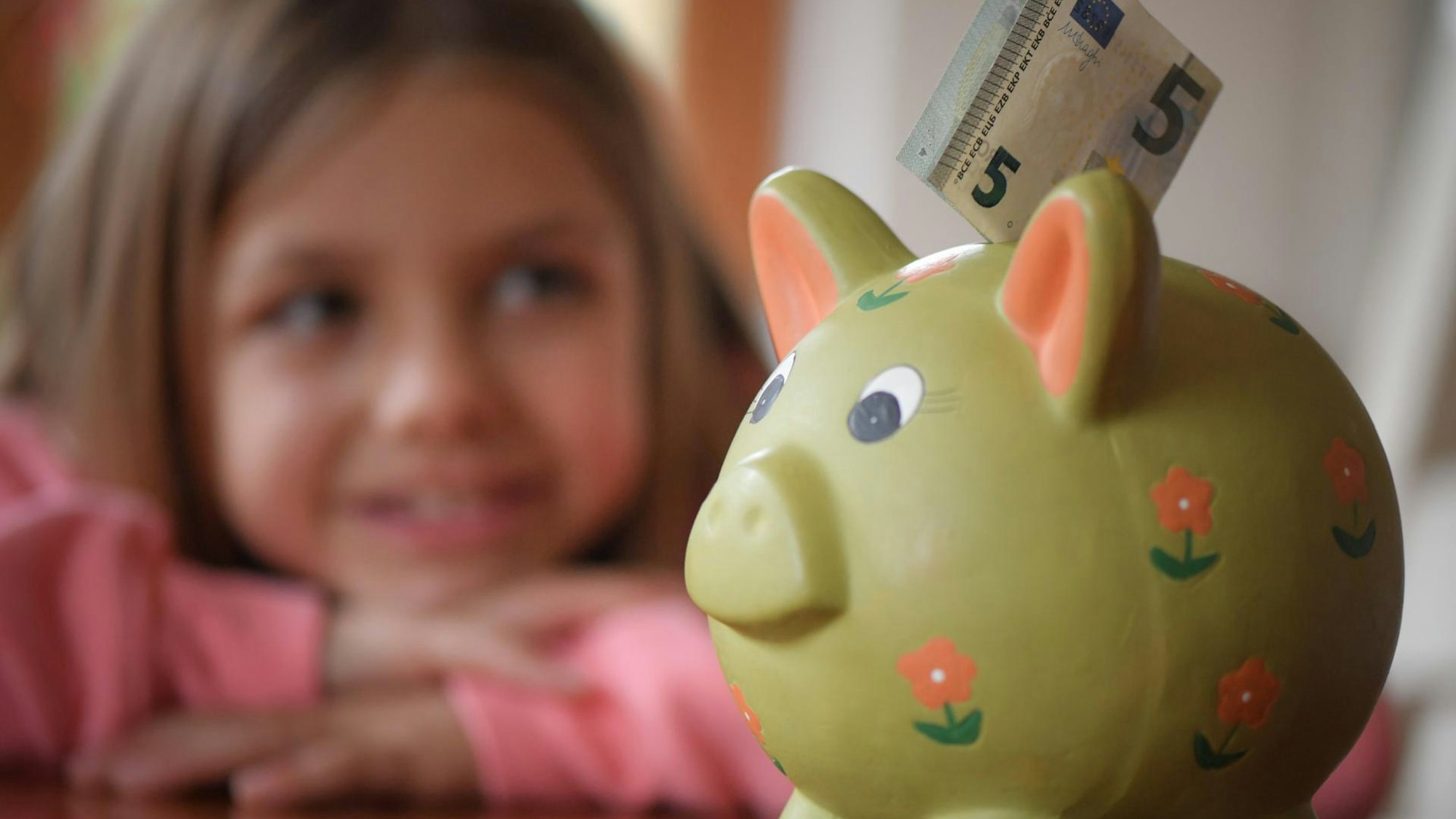 Kleines Mädchen schaut lächelnd auf Sparschwein