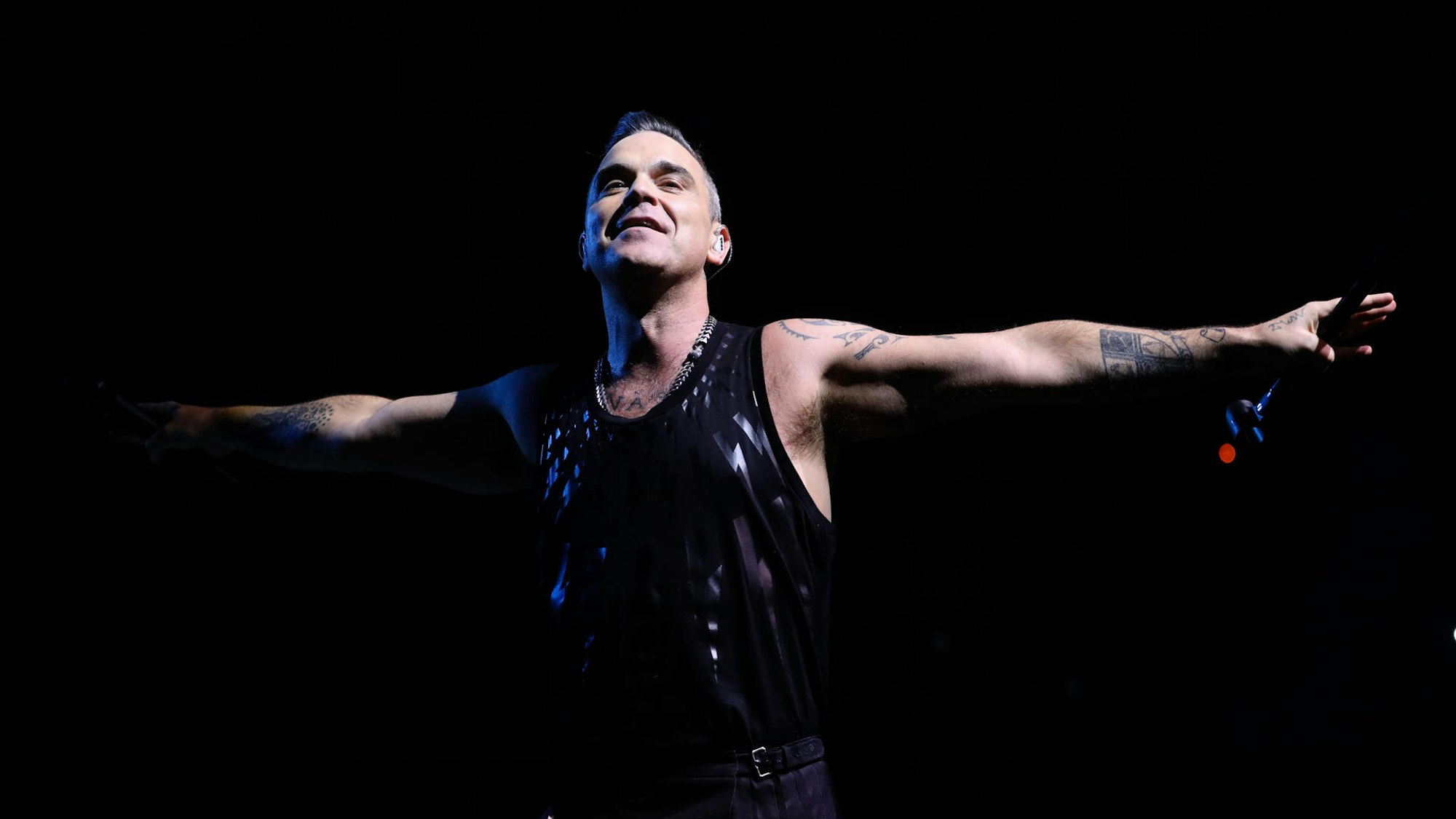 Robbie Wiliams steht mit ausgebreiteten Armen auf der Bühne.