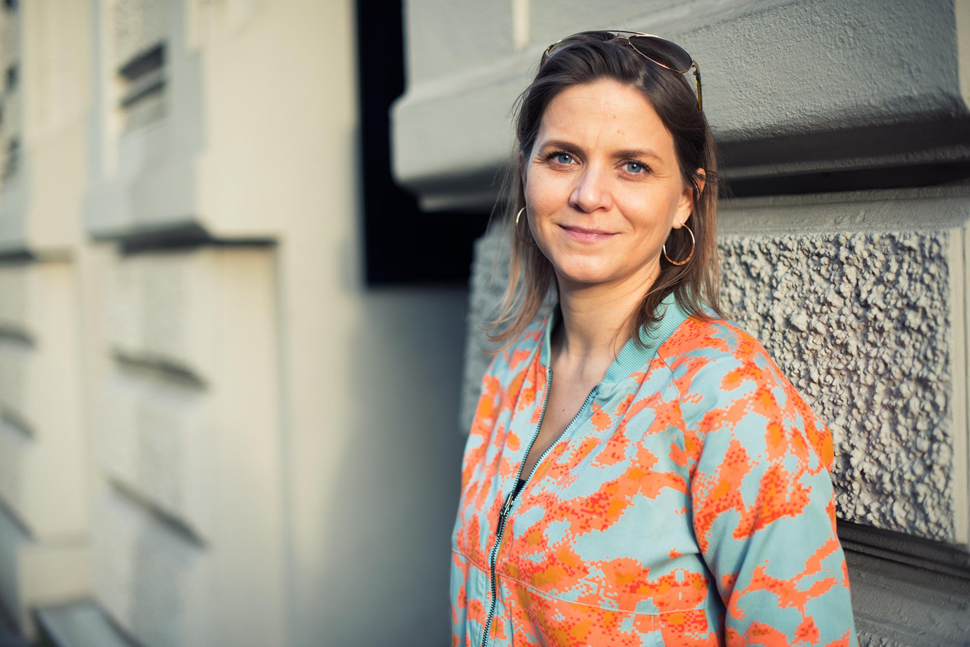 Sandra Schneeloch, Stadträtin der Grünen, steht vor einer Hauswand. Sie trägt eine ins Haar gesteckte Sonnenbrille.