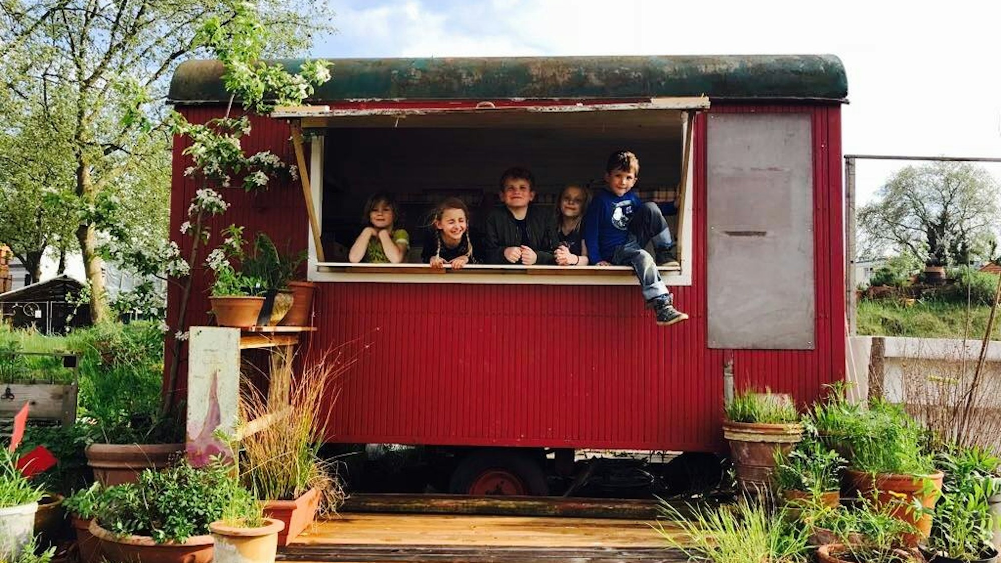 Kinder schauen aus dem Fenster eines roten Bauwagens