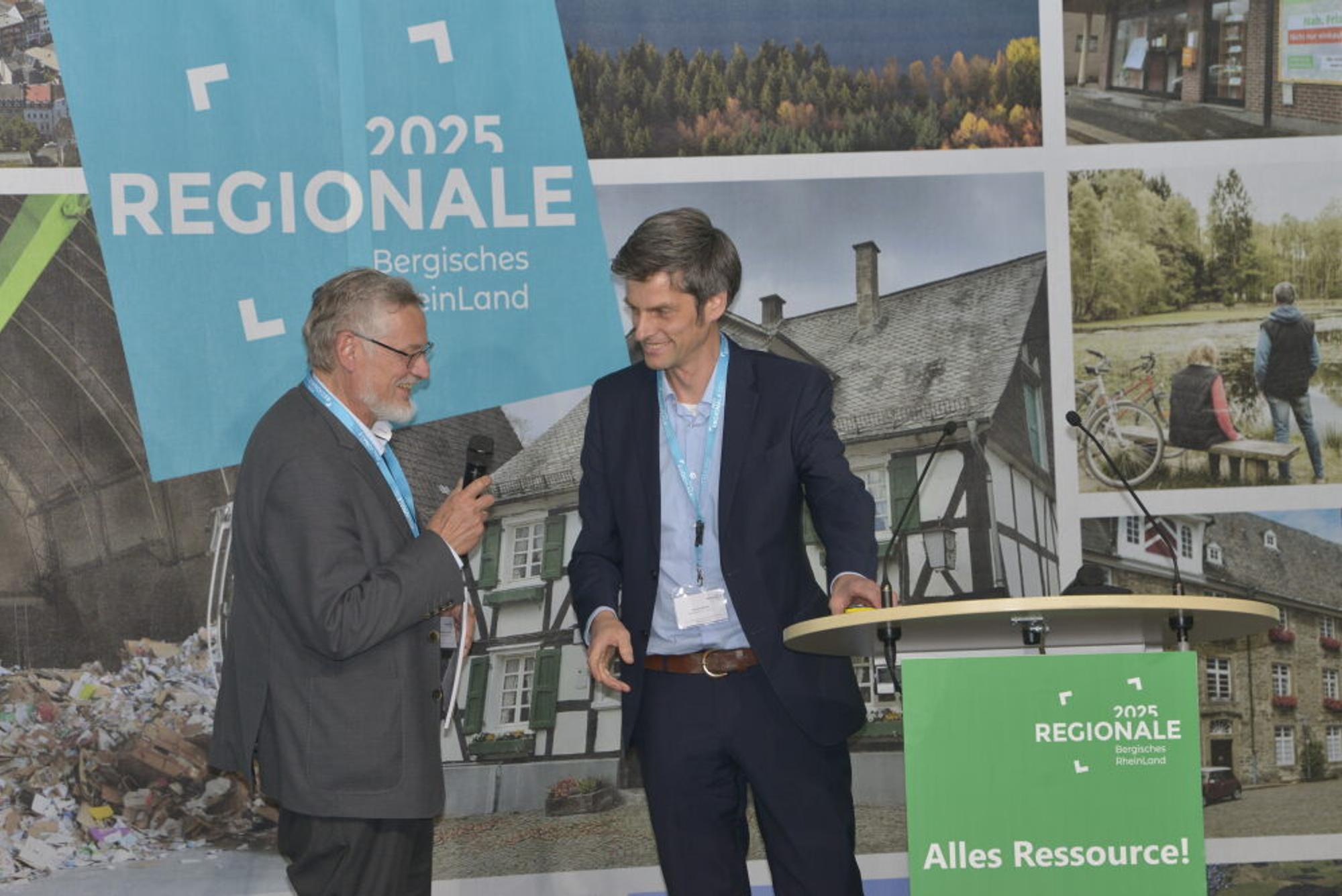 Prof. Michael Narodoslawsky (l.) und Thomas Kemme von der Regionale 2025-Agentur stehen auf einer Bühne und ziehen ein Fazit zur Veranstaltung.