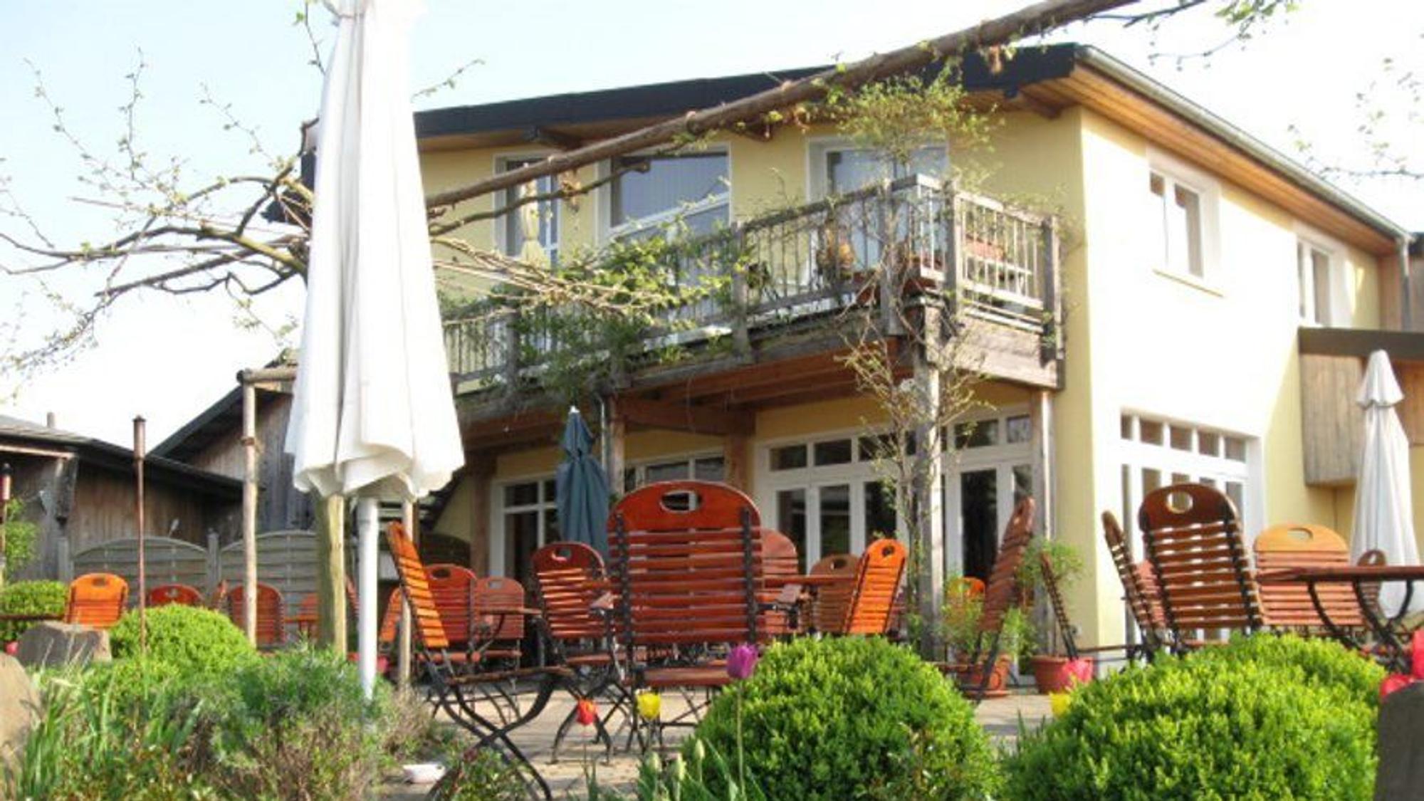 Terrasse mit Tischen und Stühlen vor einem gelben Haus mit Balkon