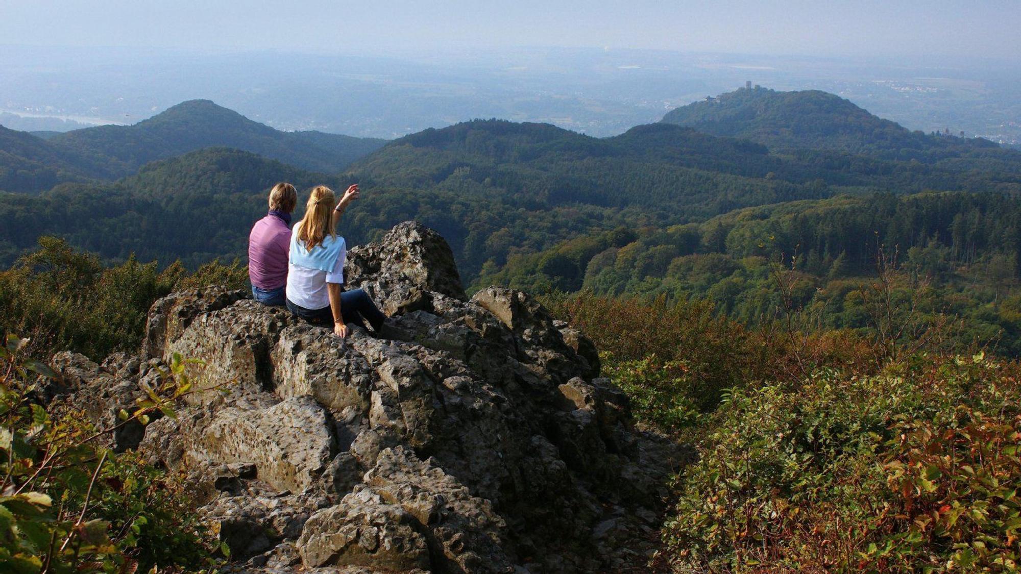 Zwei Wanderer sitzen auf einem Stein und schauen in die Ferne.