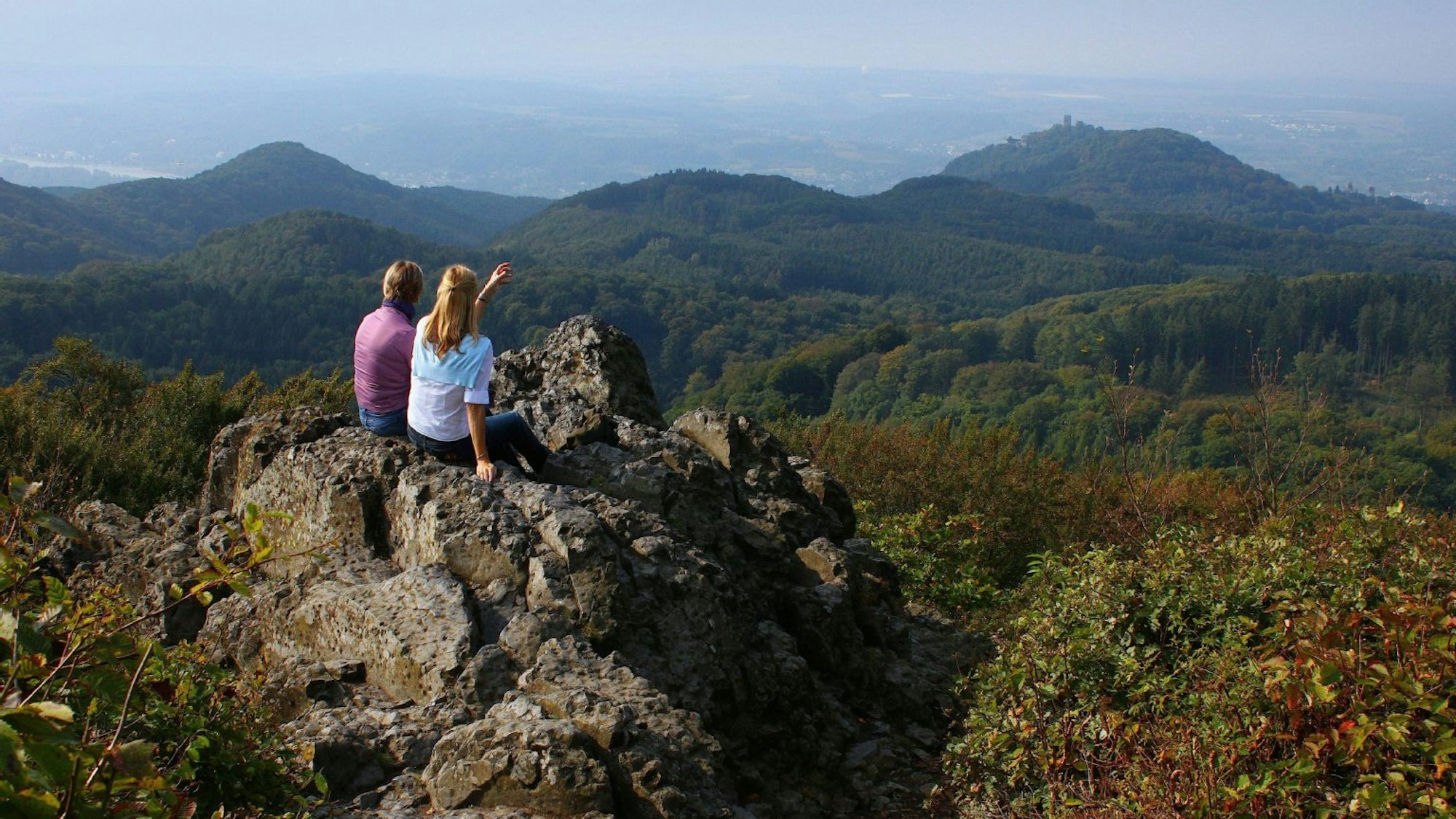 Zwei Wanderer sitzen auf einem Stein und schauen in die Ferne.