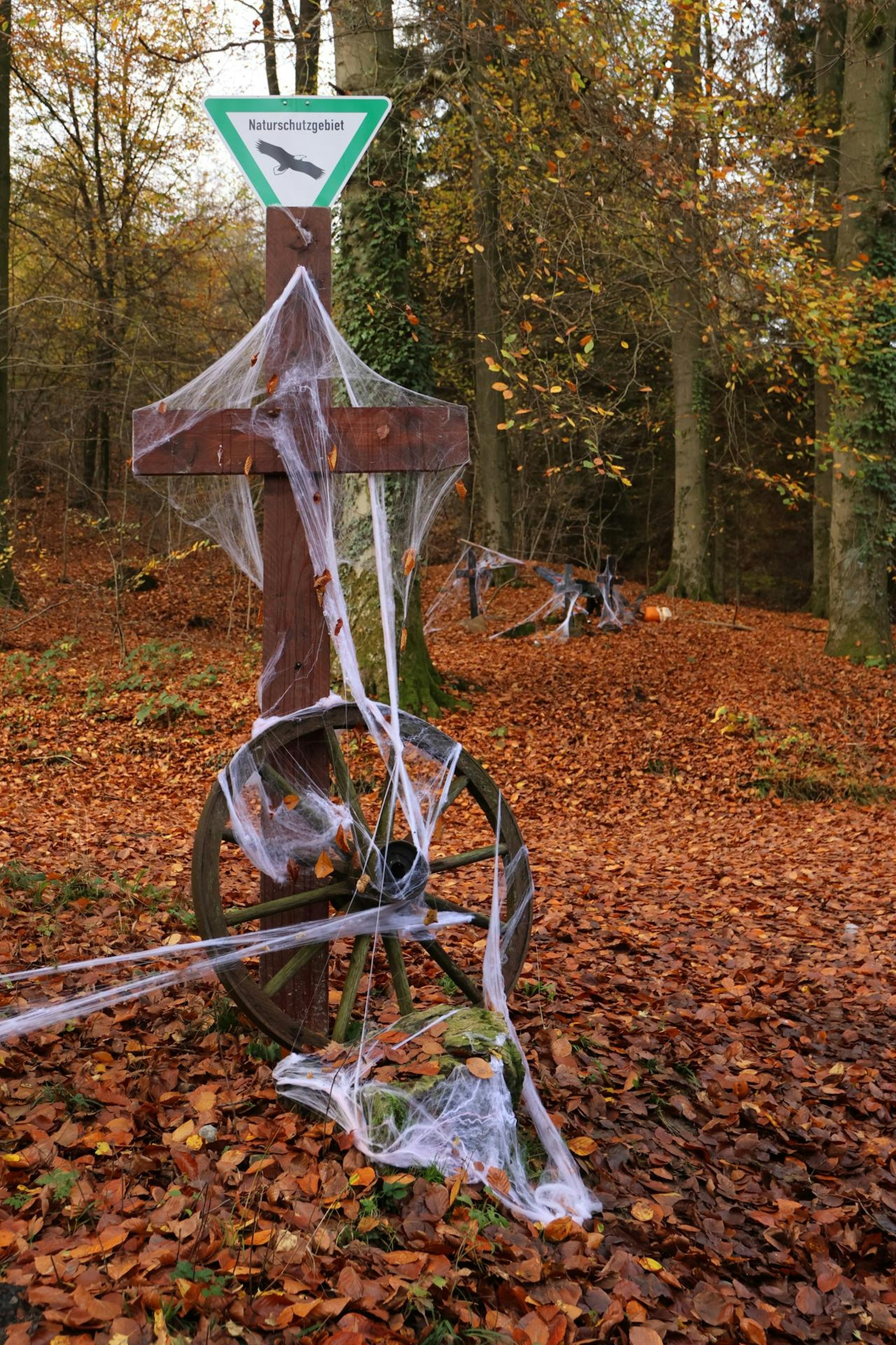 An einem Holzkreuz kleben künstlichen Spinnweben.