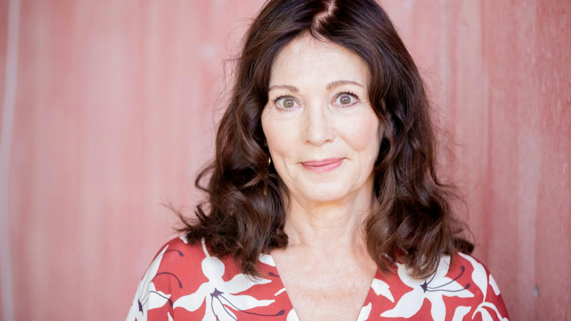 Iris Berben lächelt leicht in die Kamera. Sie trägt eine Blumen-Muster-Bluse.