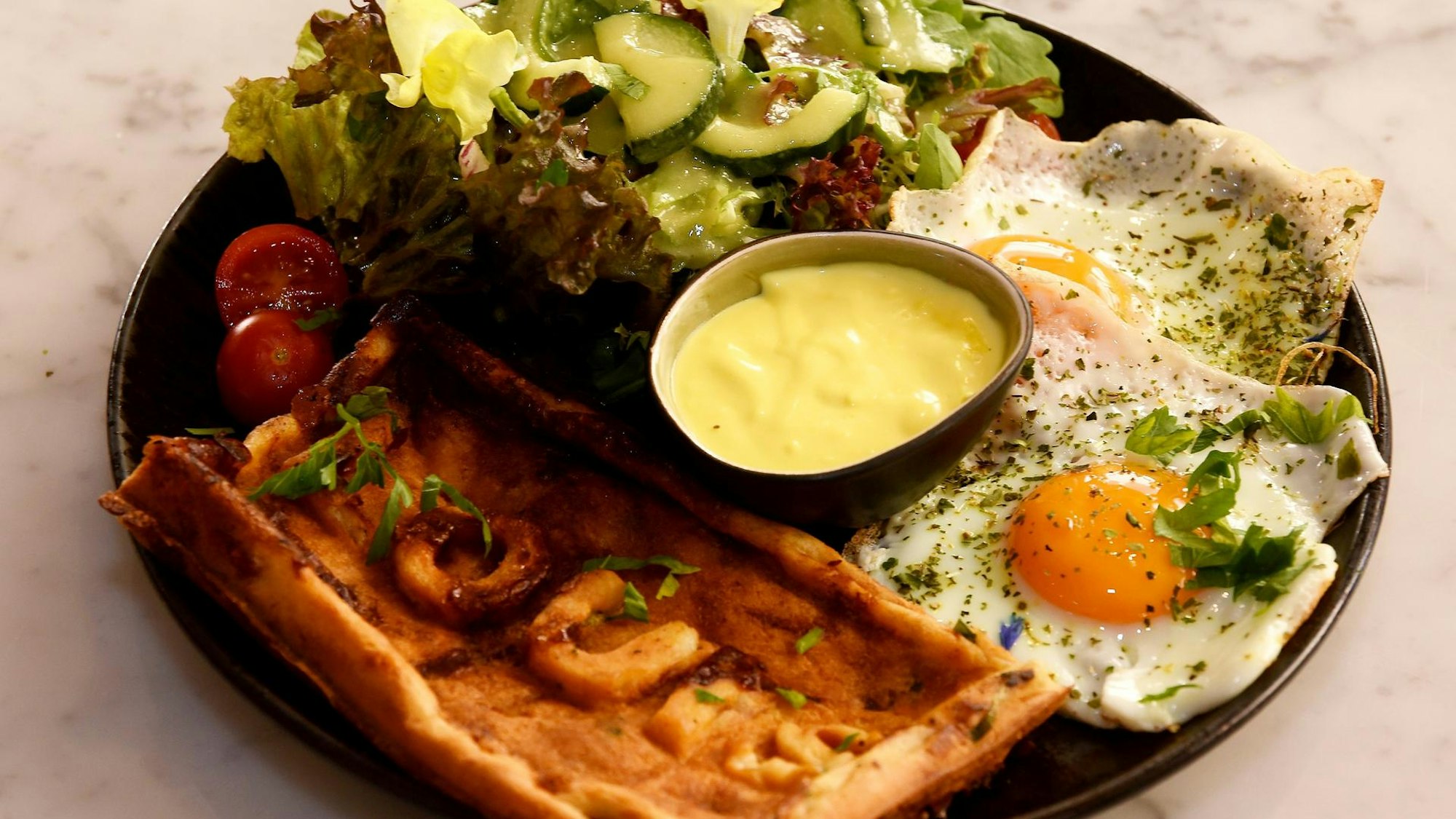 Eine herzhafte Waffel mit Salat, Hollandaise-Sauce und zwei Spiegeleiern, serviert auf einem Teller.