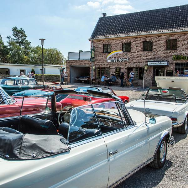 Oldtimer stehen auf einem Platz vor einer Gaststätte.