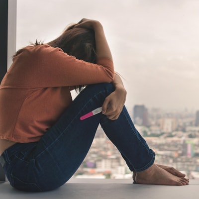 Eine Frau ist traurig und hält einen Schwangerschaftstest in der Hand.