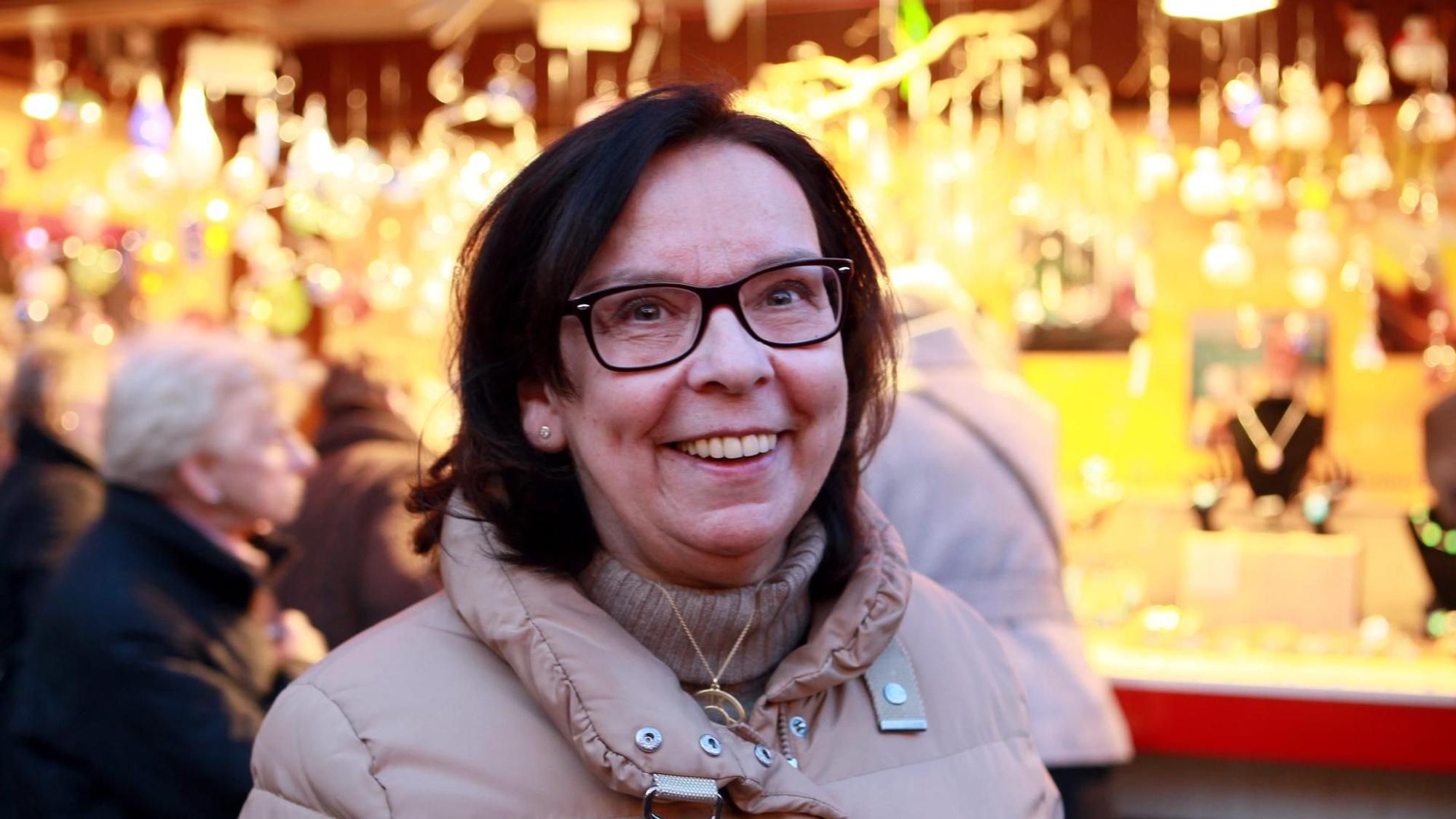 Weihnachtsmarkt-Chefin Monika Flocke steht vor einem erleuchtenden Stand auf dem Weihnachtsmarkt am Köln Dom.