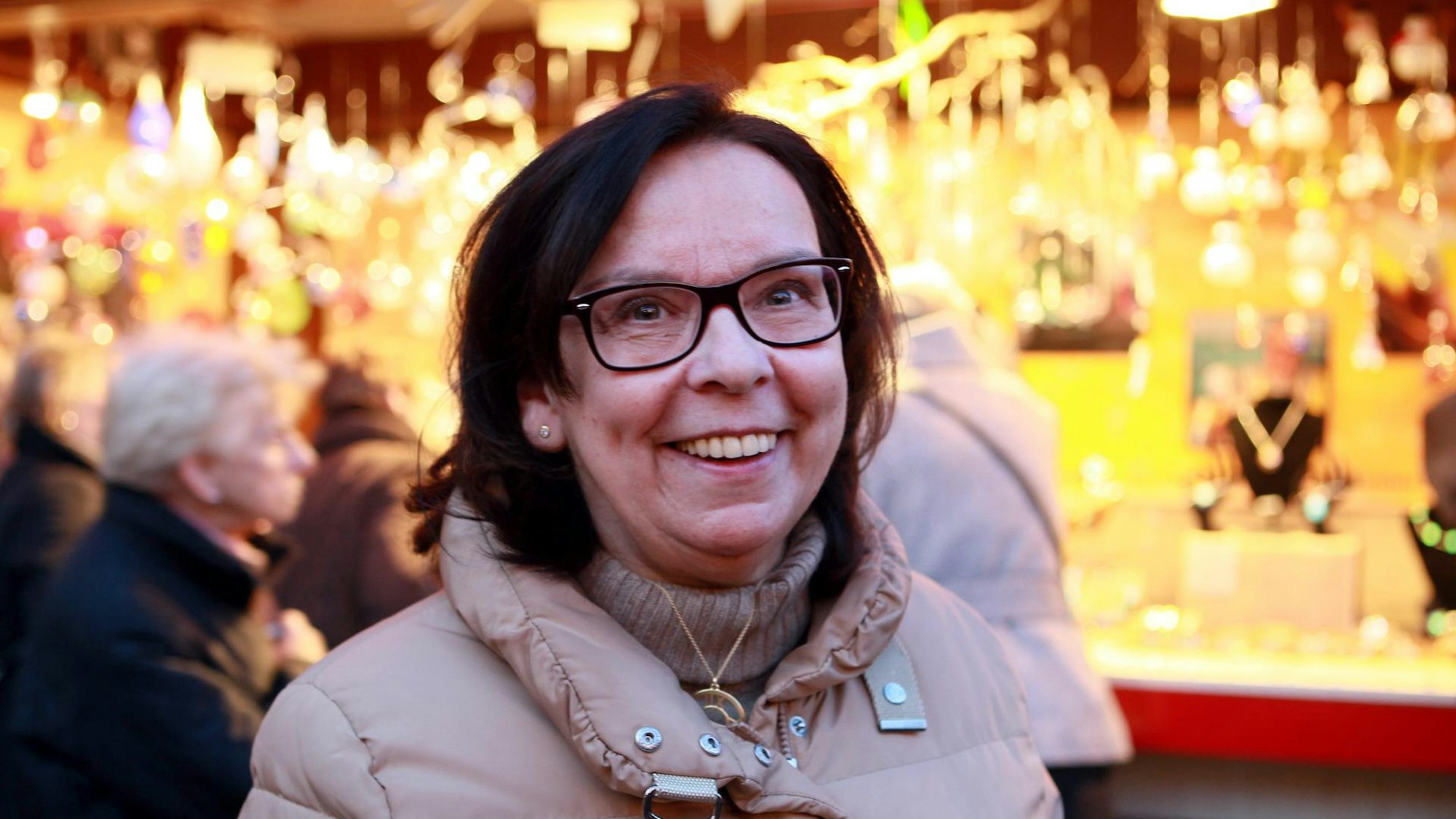 Weihnachtsmarkt-Chefin Monika Flocke steht vor einem erleuchtenden Stand auf dem Weihnachtsmarkt am Köln Dom.