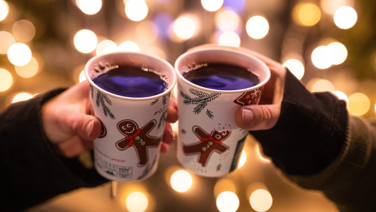 Zwei Hände tragen Weihnachtsbecher mit dem Glühwein.
