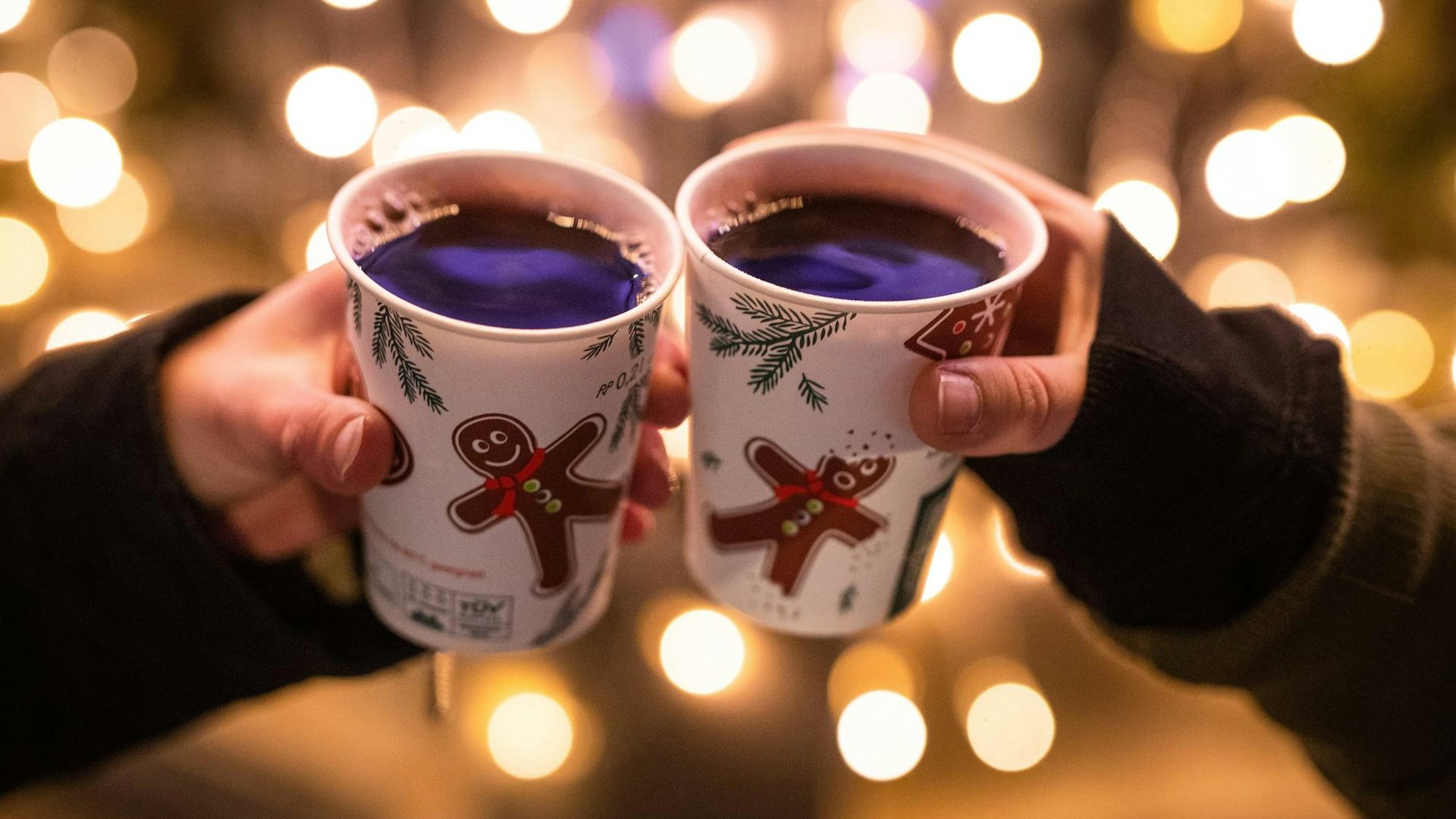 Zwei Hände tragen Weihnachtsbecher mit dem Glühwein.