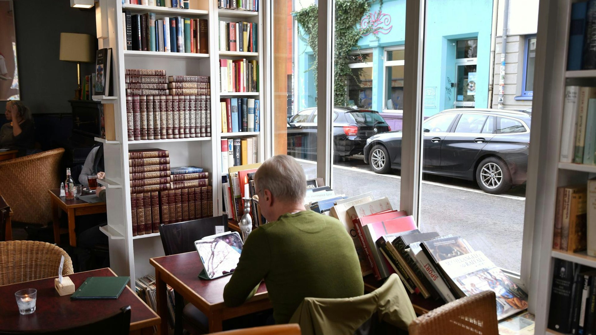 Frau sitzt an einem Tisch und liest, im Hintergrund ein Bücherregal.
