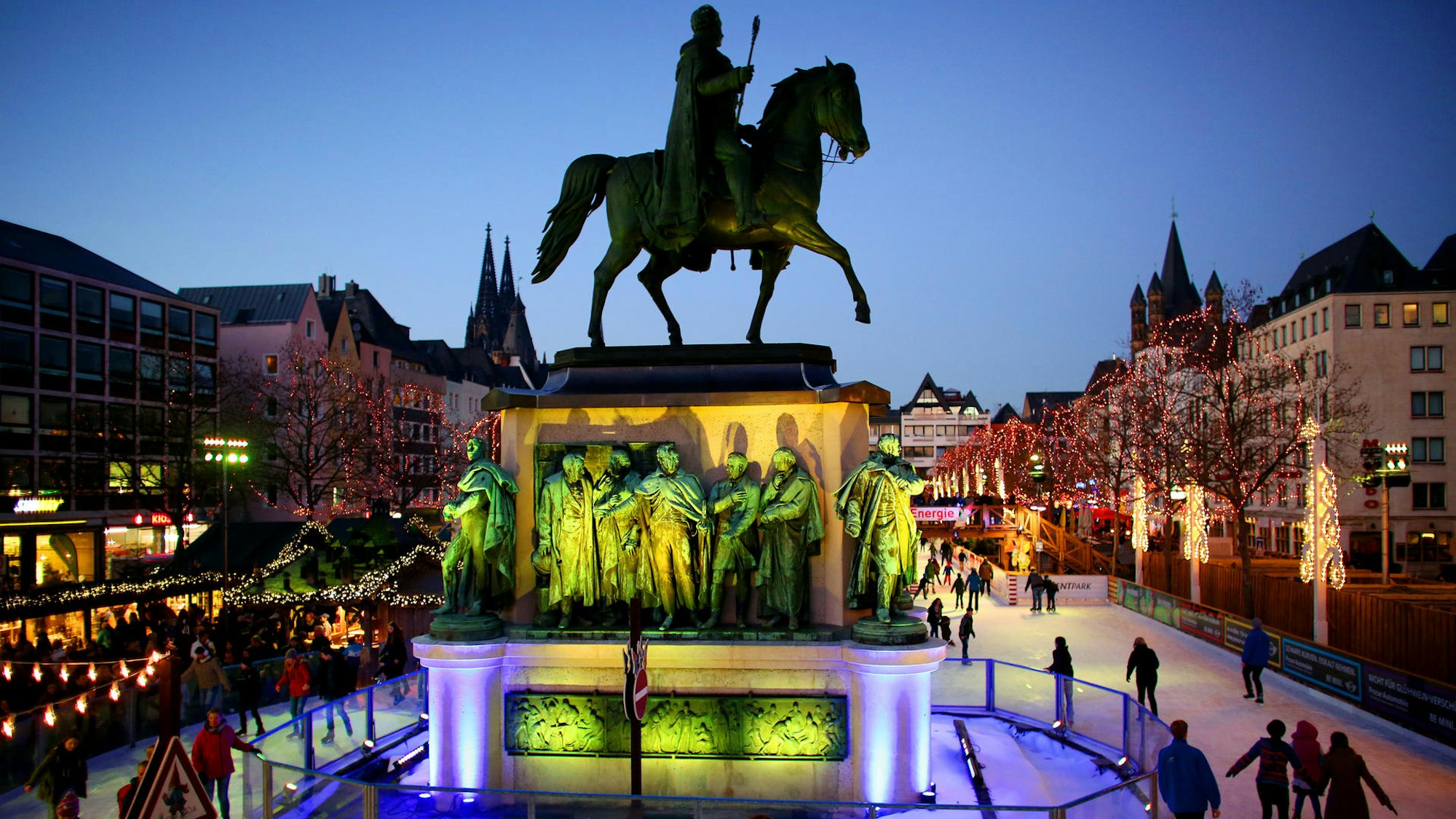 Eisläuferinnen und Eisläufer gleiten rund um das Reiterdenkmal über die Eisbahn am Kölner Heumarkt.