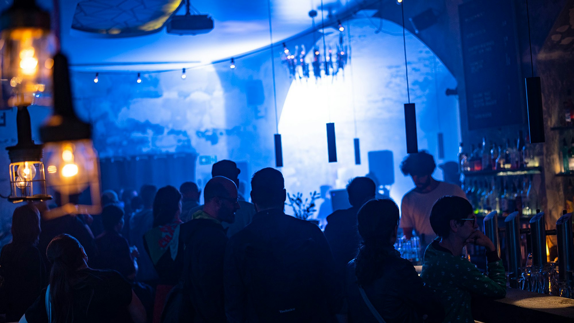 Bei schummrigen Licht sitzen und stehen Menschen im Scheuen Reh an der Bar zusammen.