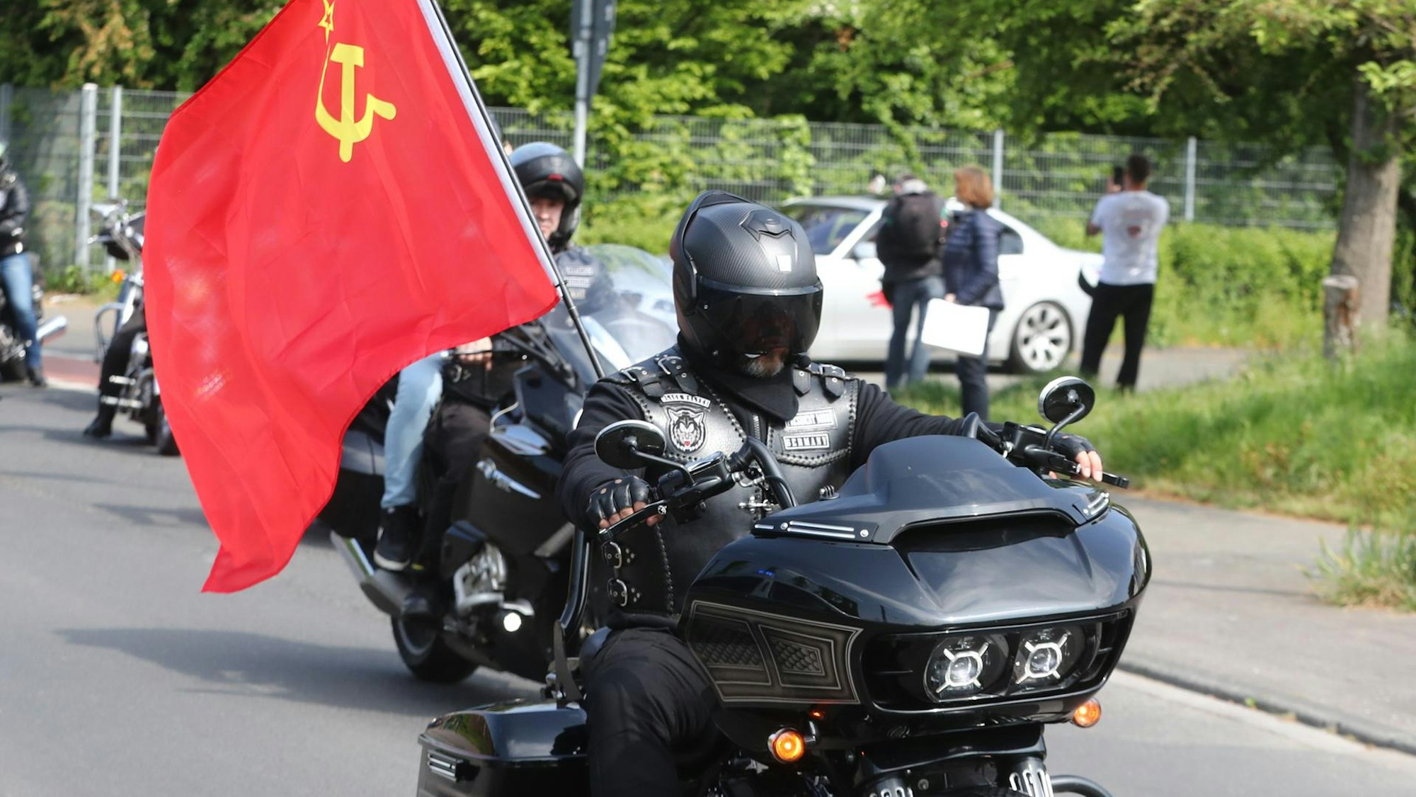 Ein in schwarz gekleideter Motorfradfahrer hat an seinem Motorrad eine sowjetische Fahne montiert und fährt so im Mai 2022 bei einer pro-russischen Demonstration in Köln mit.