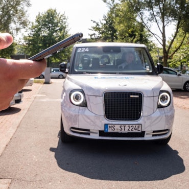 Weißer Kleinbus, davor steht ein Mann, der den Bus per Smartphone bestellt hat.
