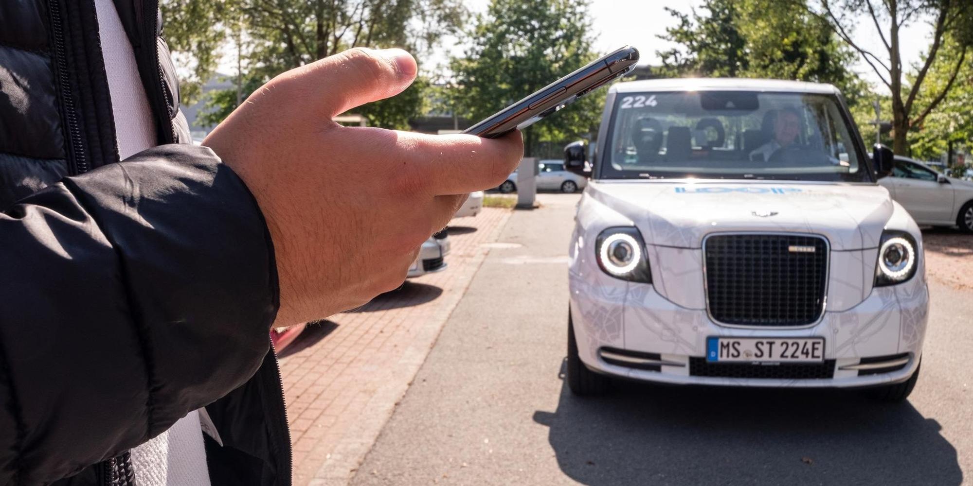 Weißer Kleinbus, davor steht ein Mann, der den Bus per Smartphone bestellt hat.