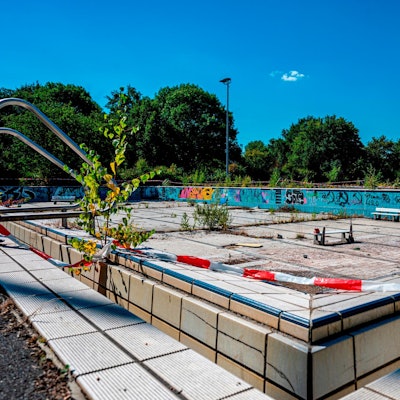 Ein verlassenes Schwimmbecken ohne Wasser. Über dem Rand liegt Absperrband.