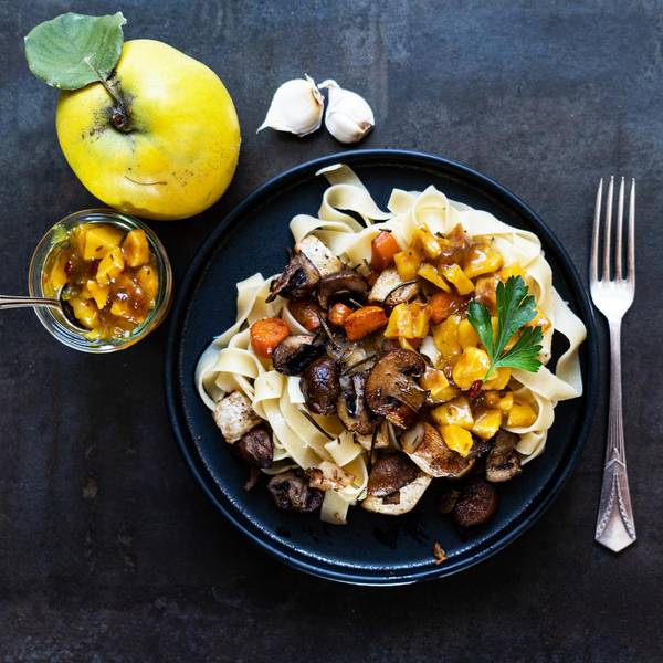 auf einem Teller liegen Fettucine, darauf Gemüse und Quitten-Stücke, links daneben liegt eine Quitte und ein Glas mit Quitten-Chutney