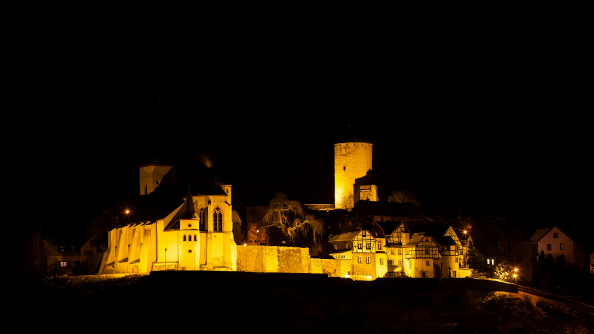 Burganlage bei Nacht in goldenem Licht angeleuchtet.
