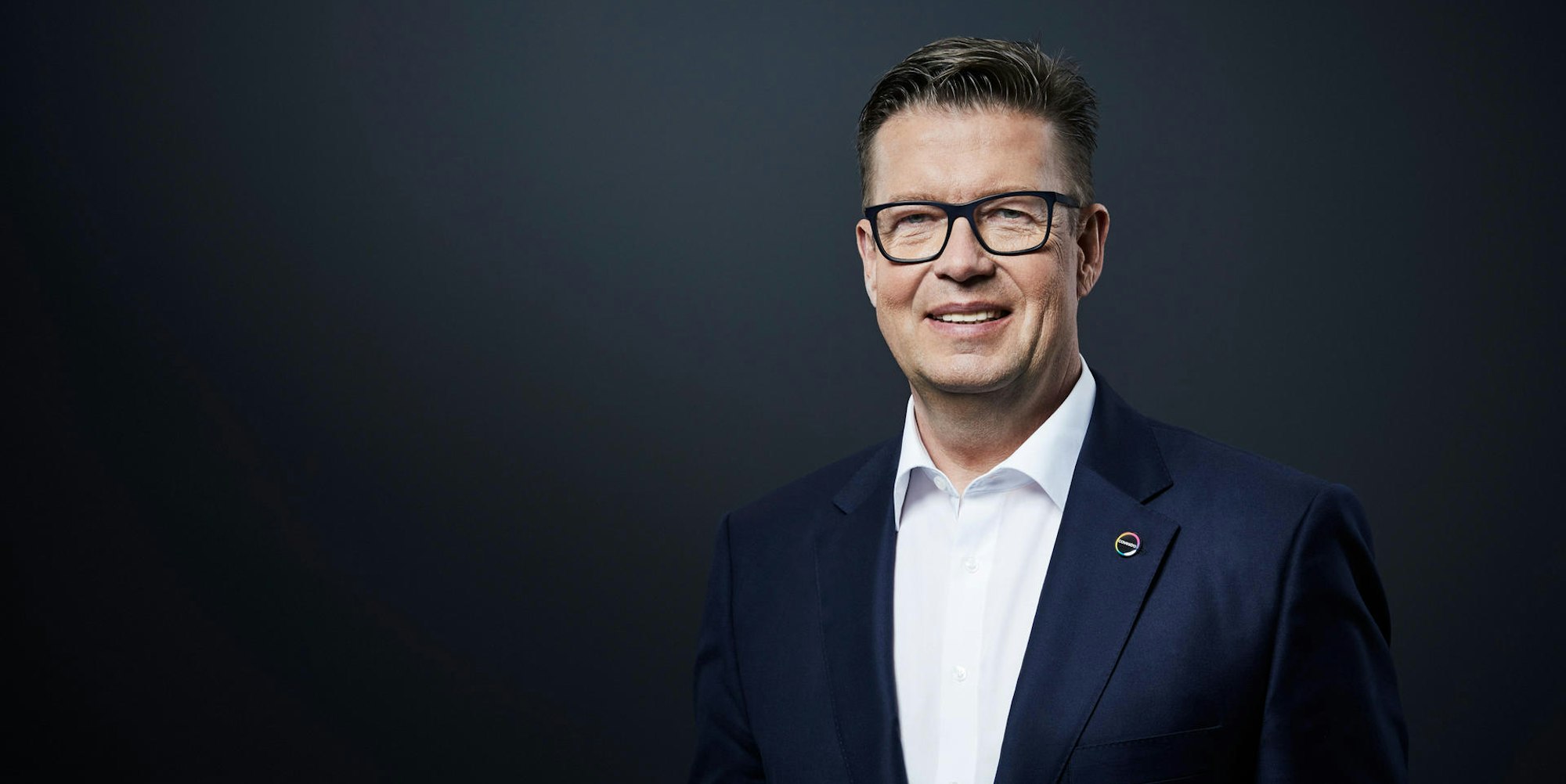 Klaus Schäfer im Anzug mit Brille vor schwarzem Hintergrund.