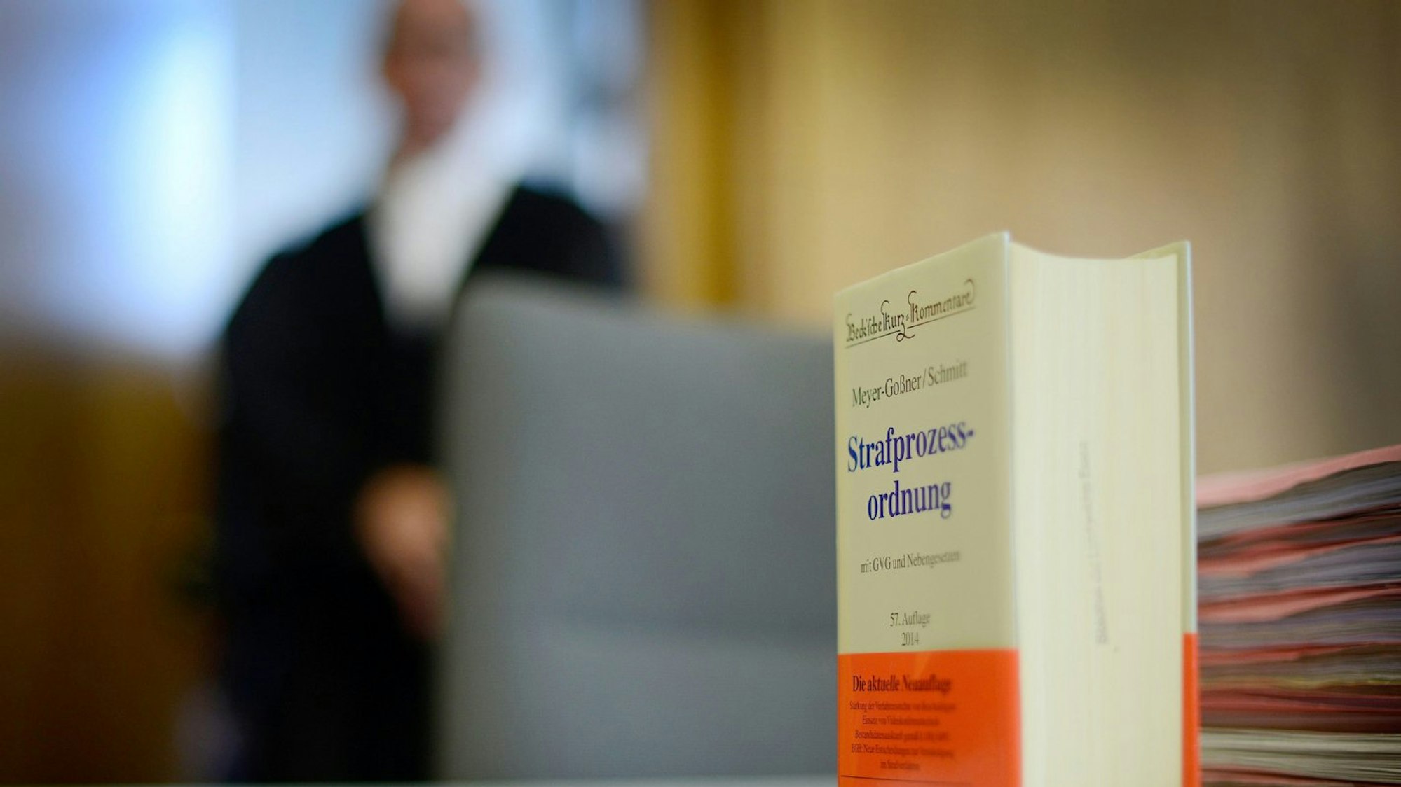 Das Buch der Strafprozessordnung steht auf einem Tisch, im Hintergrund ein Richter in Robe.