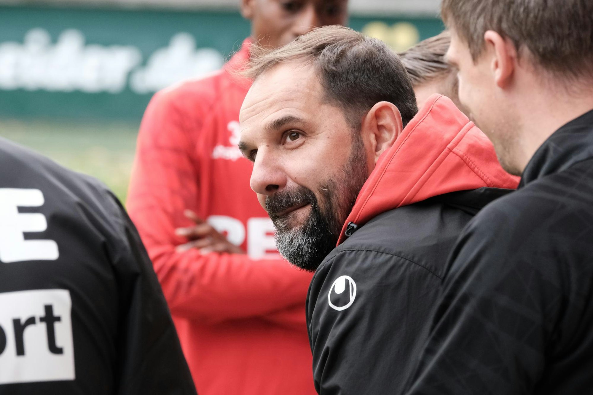 Ein Fußballtrainer steht im Kreise seiner Spieler am Rande des Platzes.