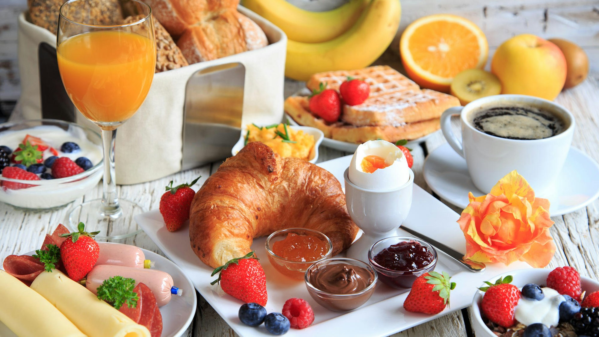 Ein Frühstückstisch mit verschiedenen Aufstrichen, Croissant, Waffeln, Orangensaft und mehr, appetitlich angerichtet