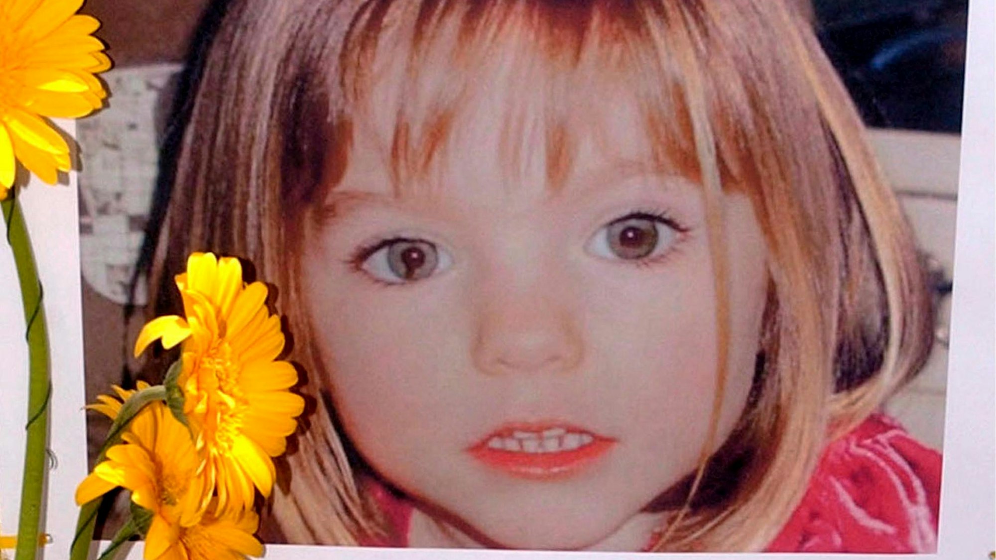 Blumen stehen vor einem Bild, das die verschwundene Madeleine McCann (Maddie) auf einem Foto zeigt, das ihre Eltern im Zusammenhang mit dem Verschwinden des Kindes veröffentlicht haben.