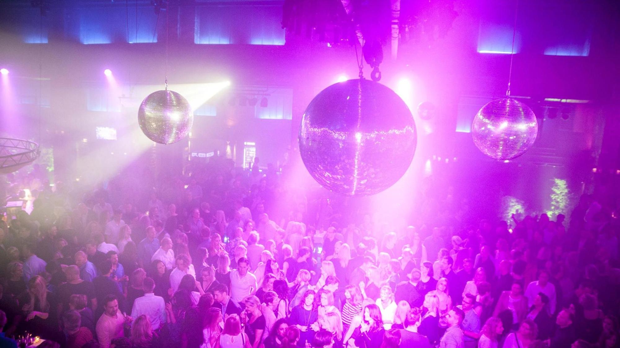 Menschen tummeln sich auf der Tanzfläche in der Halle Tor 2, sie werden von Disco-Kugeln angestrahlt.